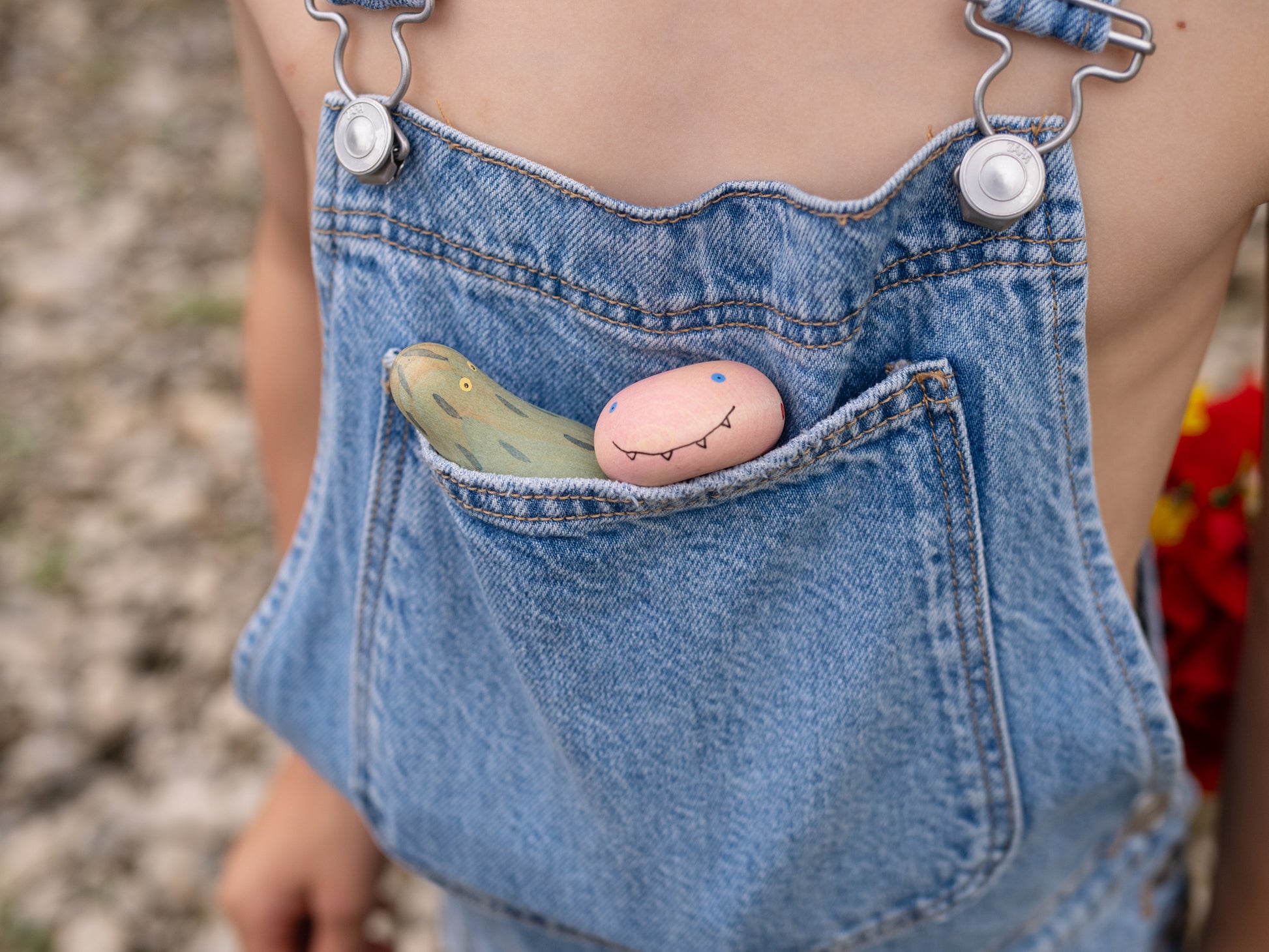 Person wearing denim overalls with decorative stones in the pocket against a blurred natural background