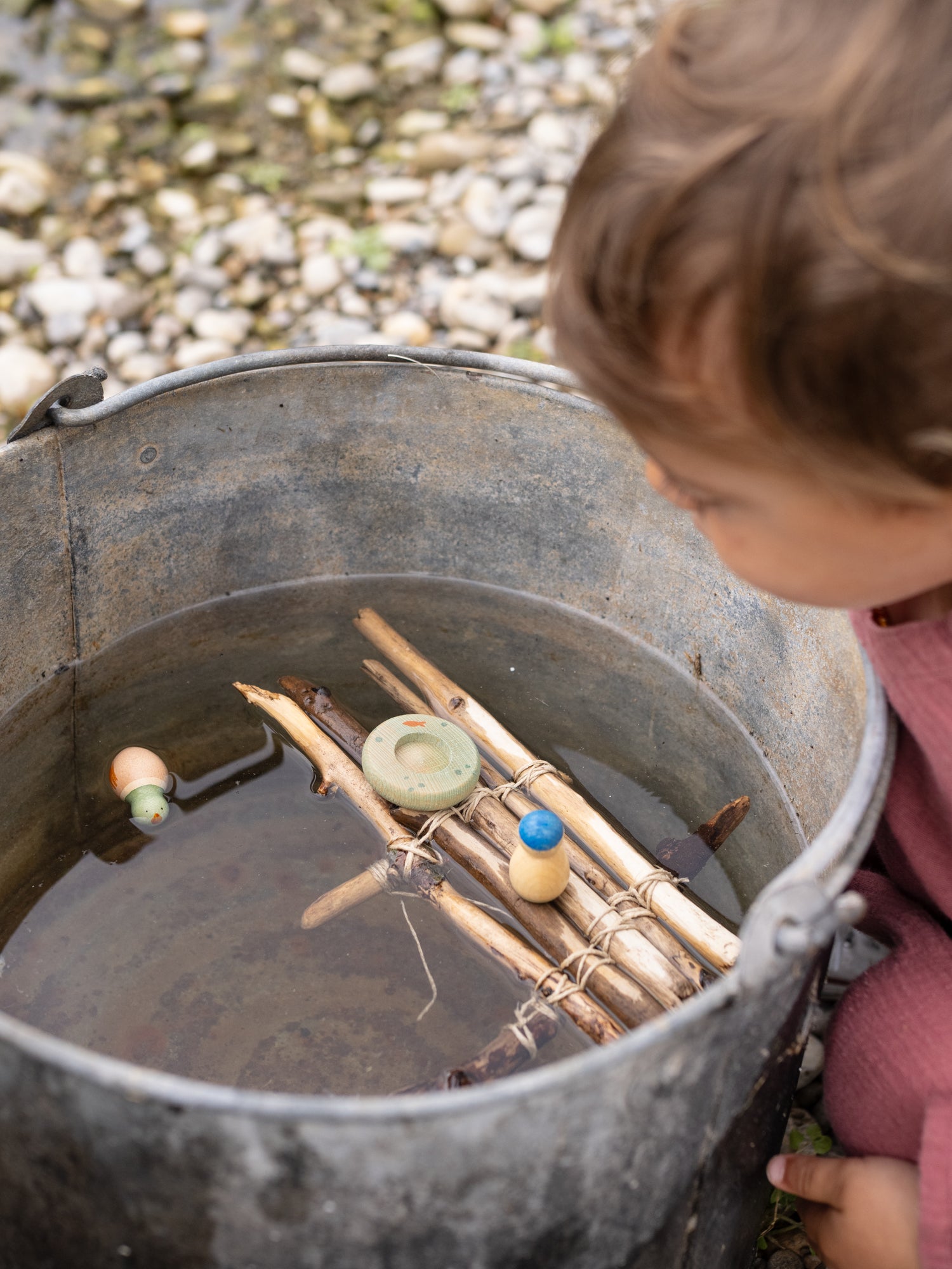 Child looking into a bucket with sticks and stones