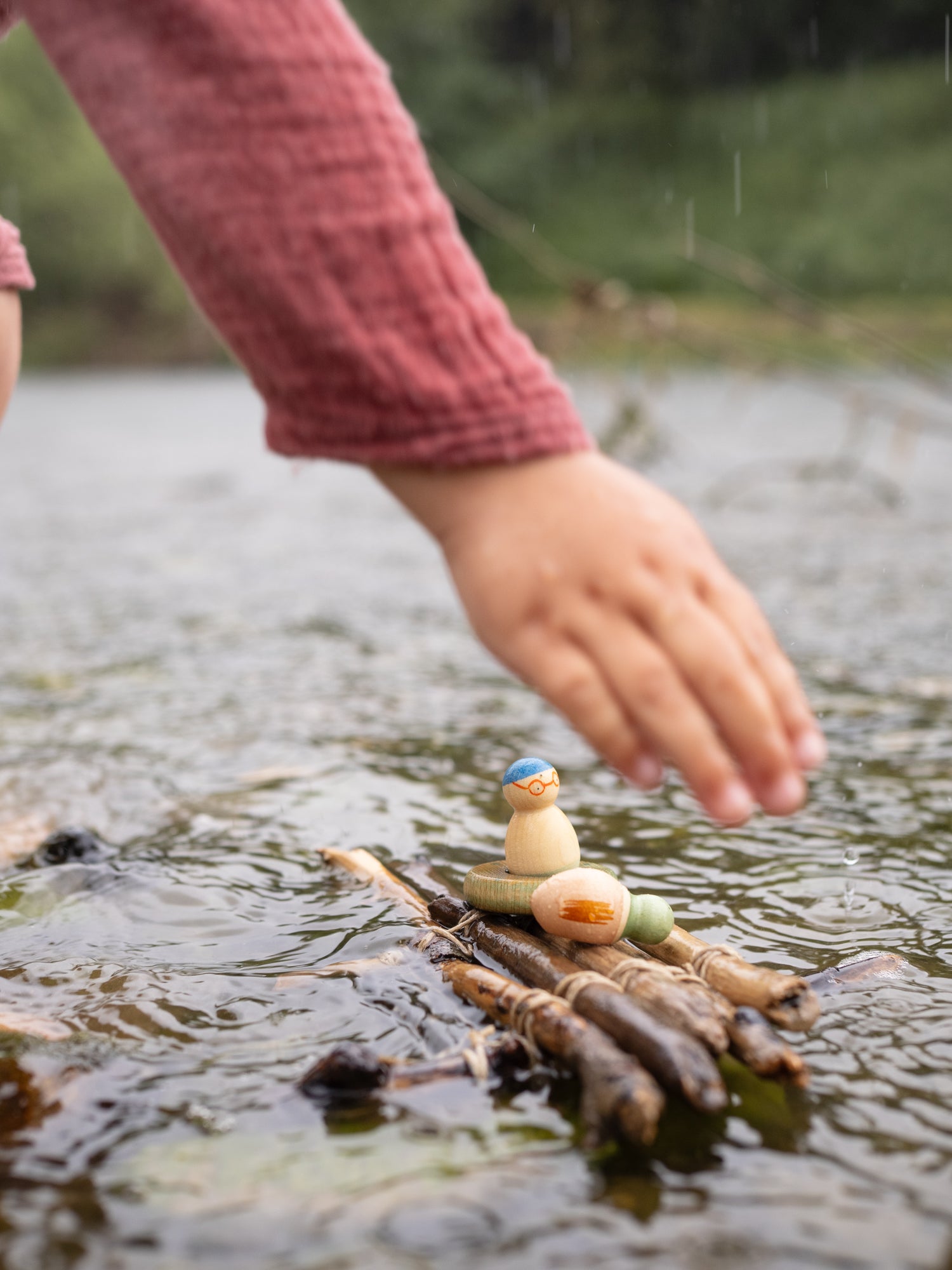 Hand reaching towards a toy duck on sticks in water