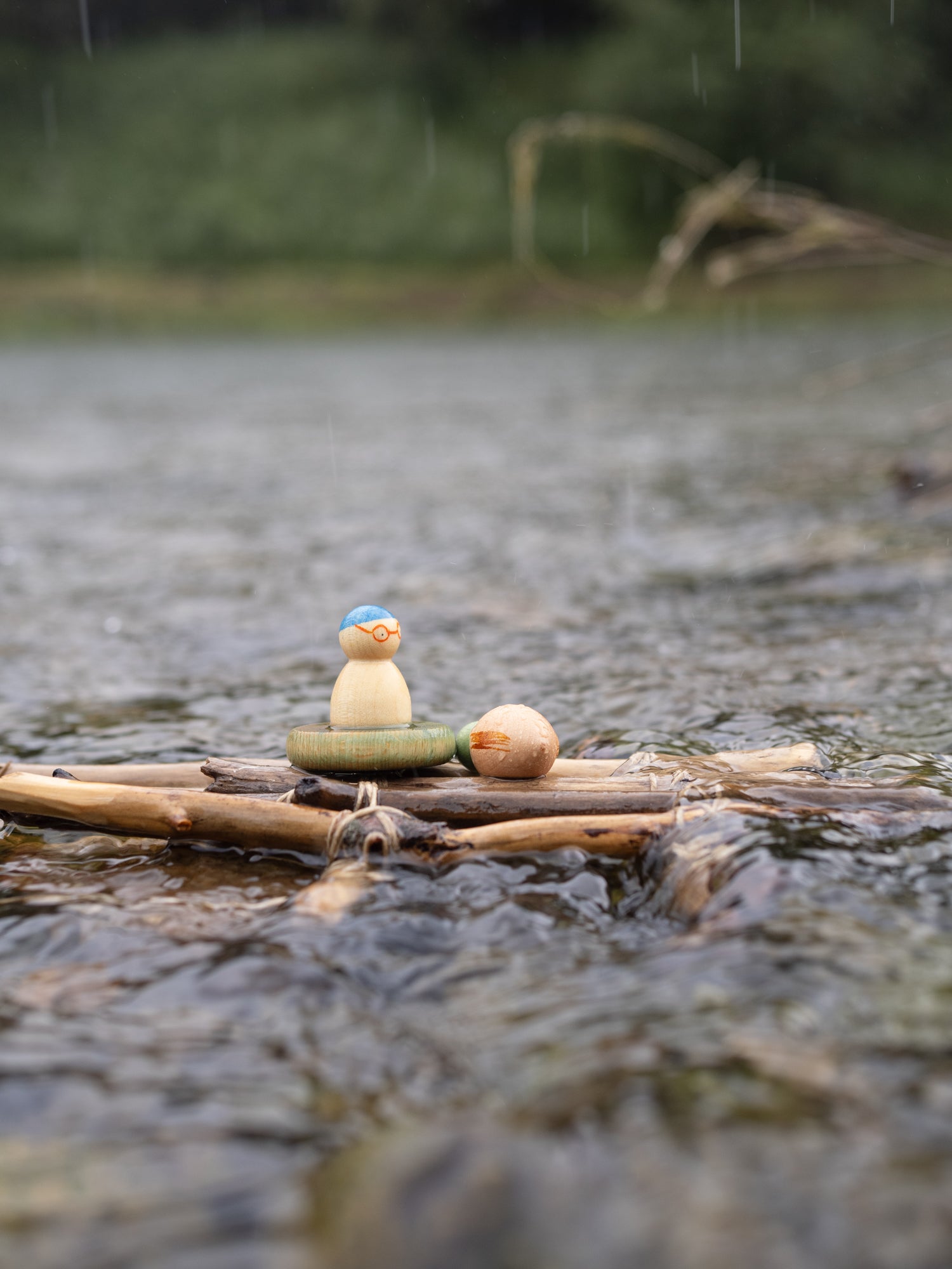 Small figurine on a log floating in water with a blurred natural background