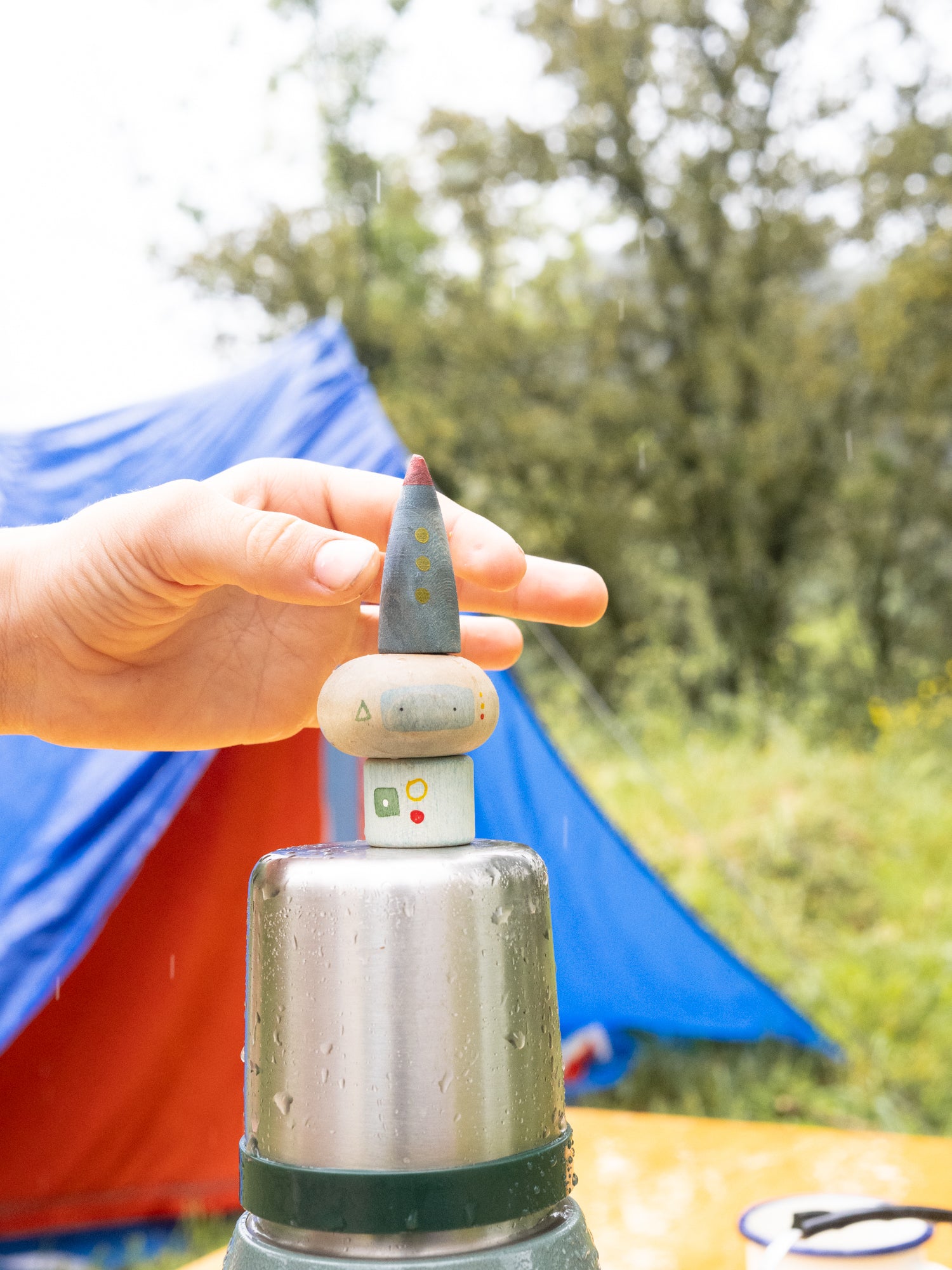 Hand holding a small wooden object with a blurred outdoor background