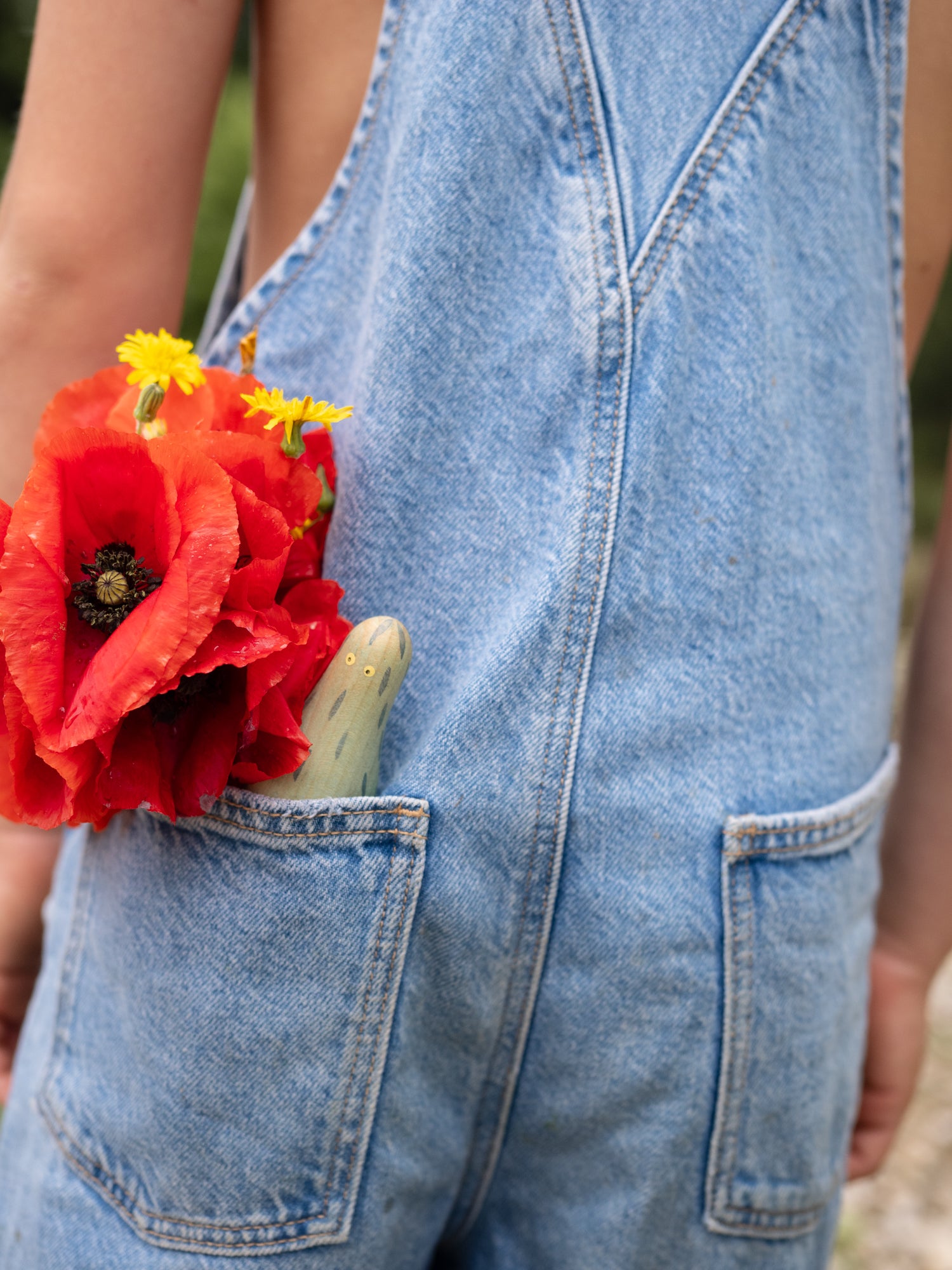 Person wearing denim overalls with a red flower in the pocket