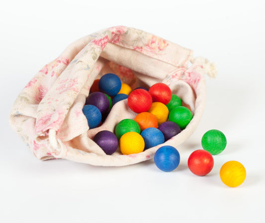 Colorful wooden toy marbles spilling out of a floral-patterned bag on a white background