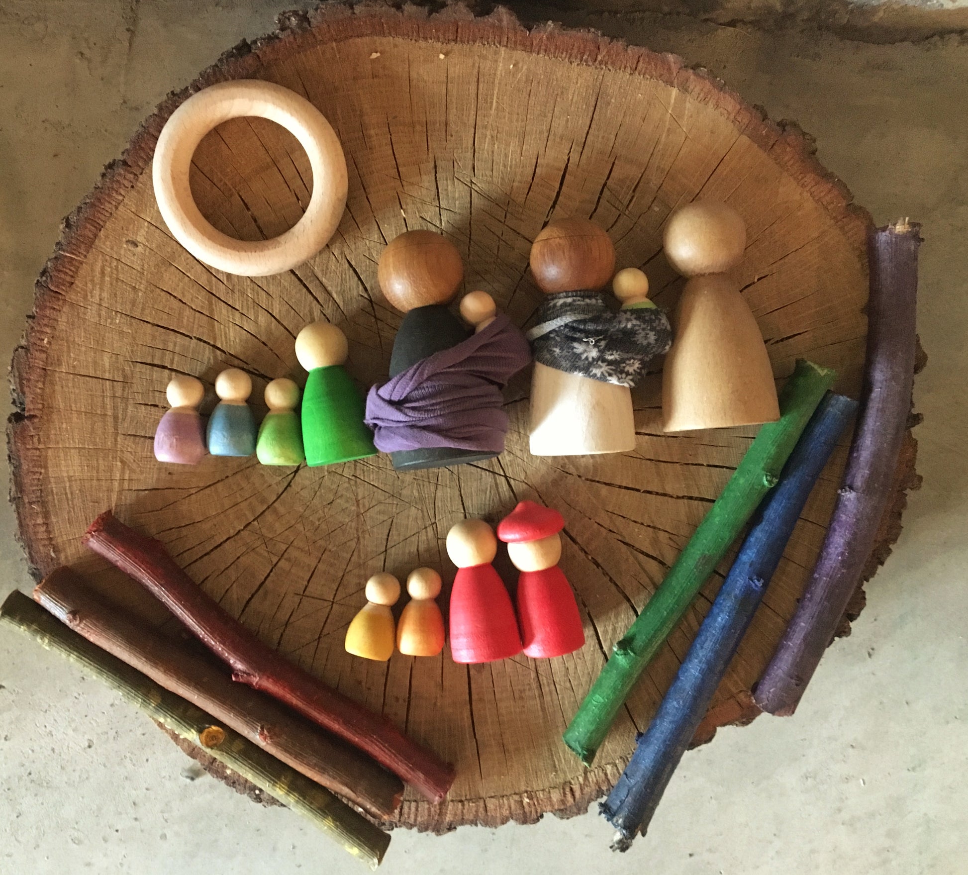 Wooden toy peg dolls on a log with natural materials