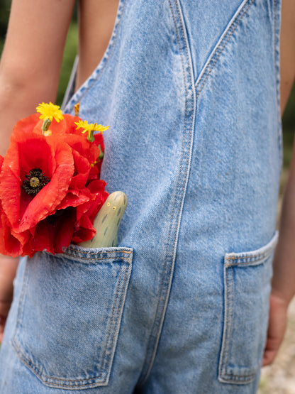 Person wearing denim overalls with a red flower in the pocket