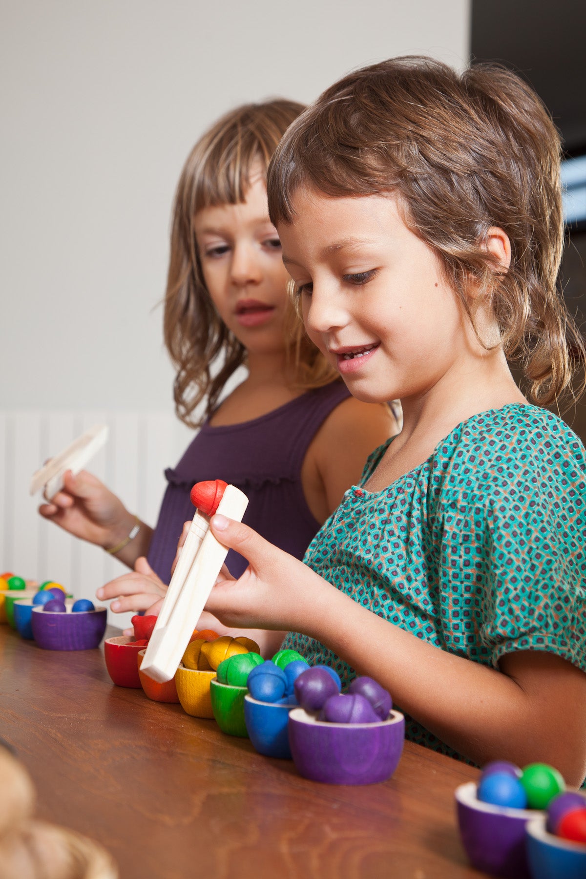 Children using wooden tweezers to pick colourful wooden acorns out of small colourful bowls 