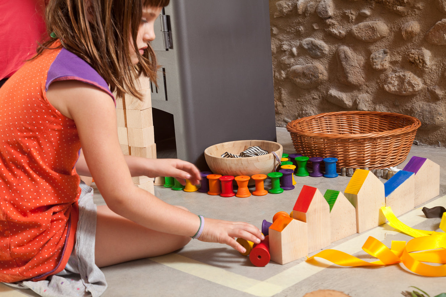Child playing with wooden toy houses alongside other wooden toys