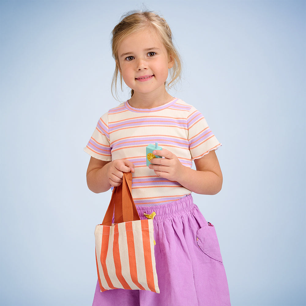 Child holding fabric bag containing wooden toy groceries.