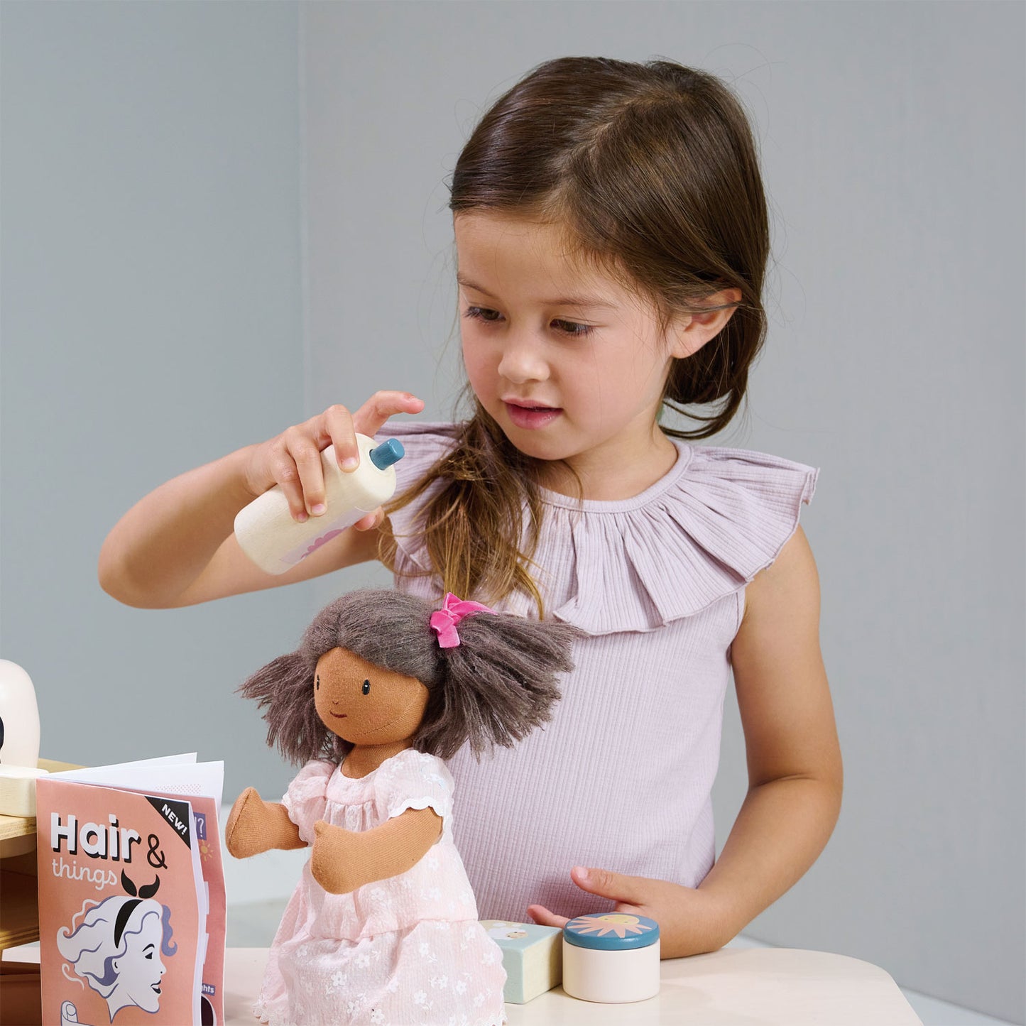 Child playing with wooden pretend play hair salon.  Spraying doll's hair.  