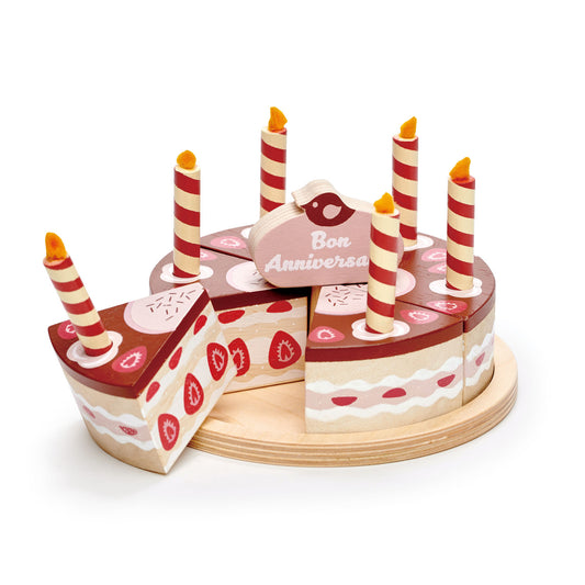 Wooden toy chocolate birthday cake with six candles and cake topper which says happy birthday.  The cake is divided into six pieces and presented on a wooden plate.  A cake slice is removed showing a strawberries and cream filling.