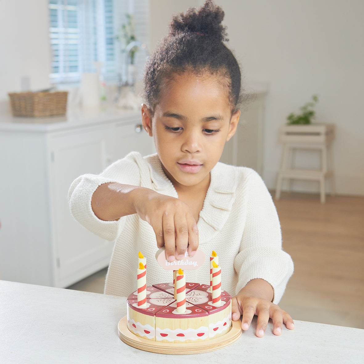 Child placing cake topper onto wooden toy chocolate birthday cake with six candles.  The cake is divided into six pieces and presented on a wooden plate.