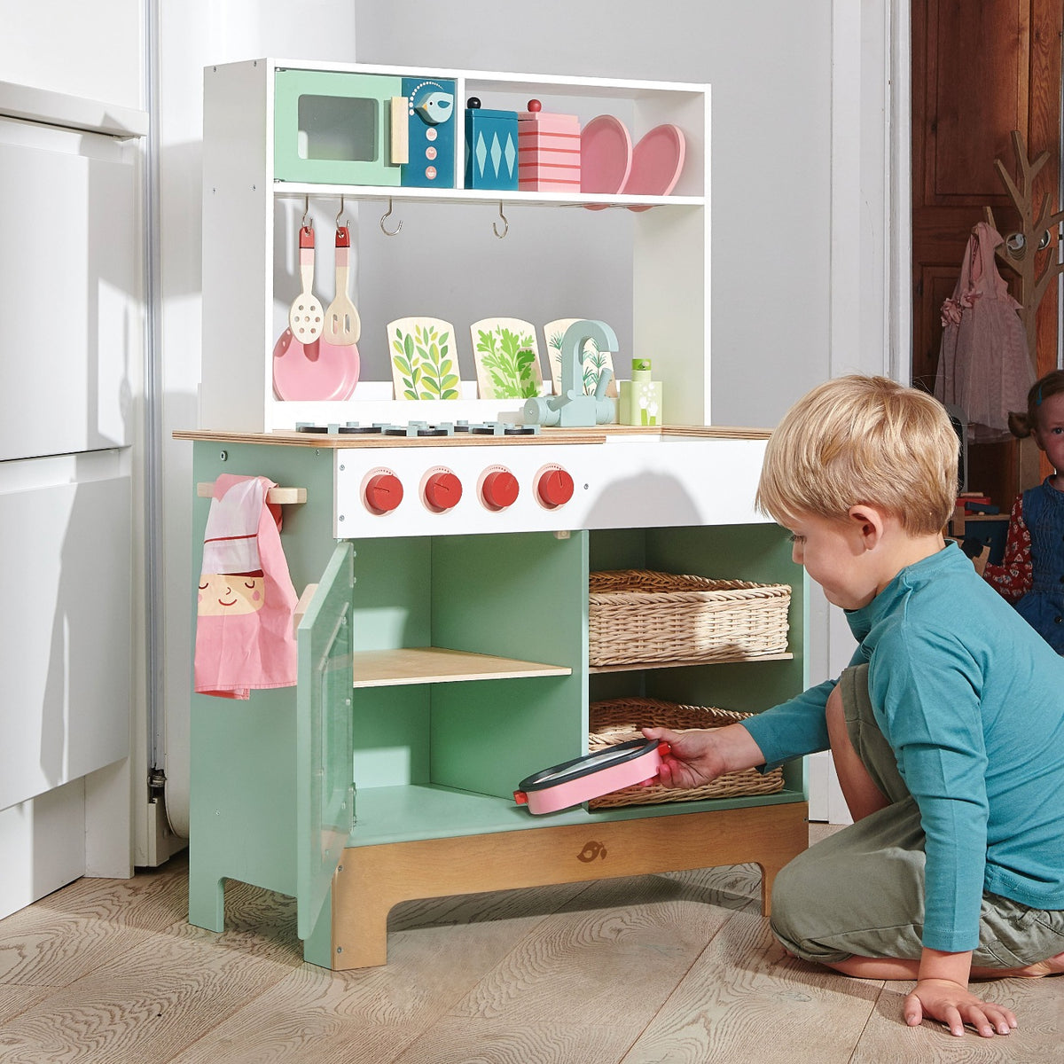 Tender Leaf Toys Kitchen Range front view showing child placing a wooden toy casserole dish into the play kitchen oven.